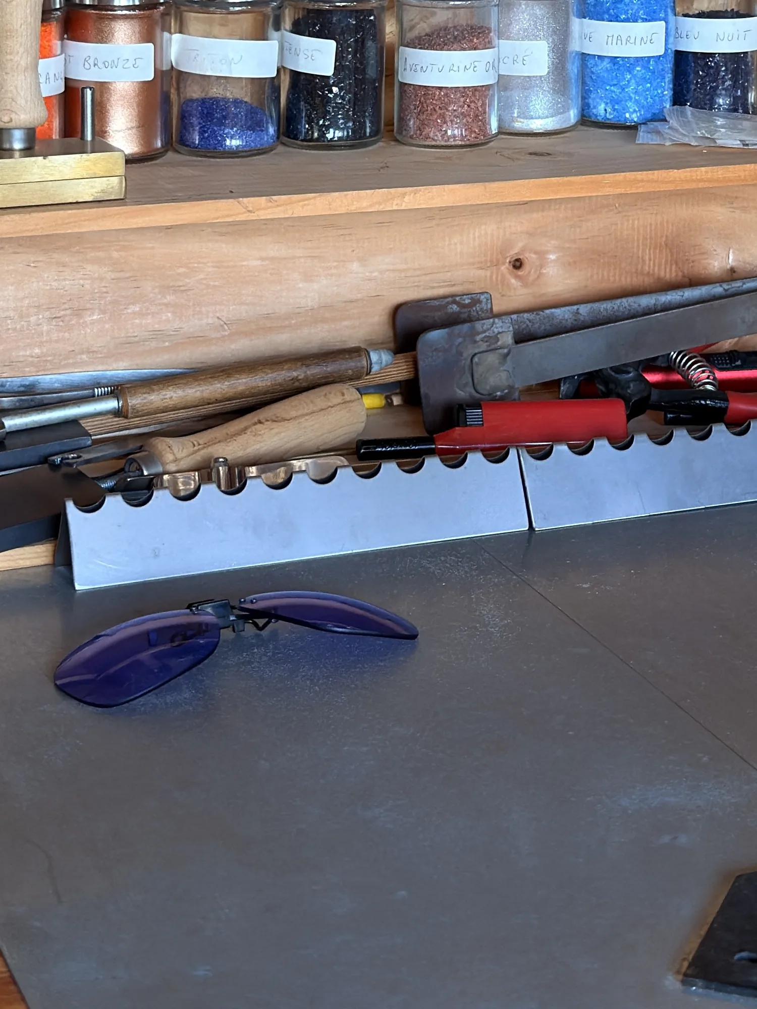 Les lunettes violettes posées sur la plaque d'acier, devant les outils et les bocaux de poudres.