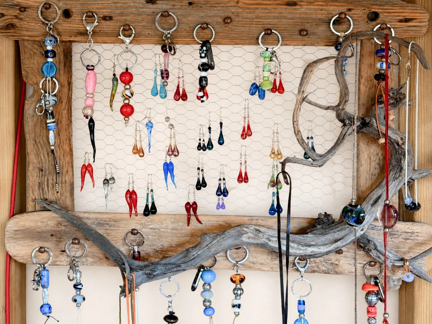 Un cadre grillagé traversé d'une branche de bois flotté, couvert de porte-clés et de boucles d'oreilles.