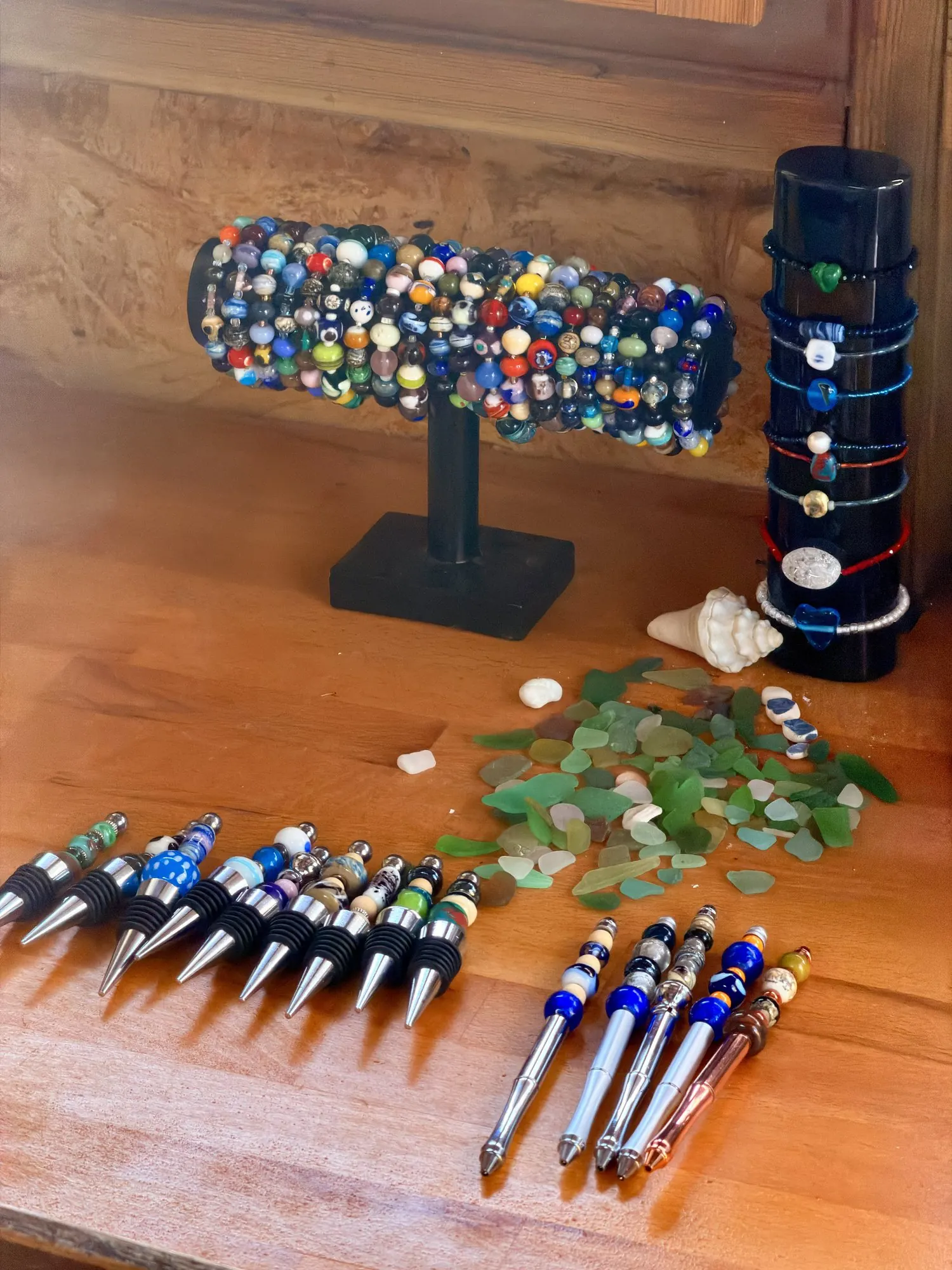 Sur l'établi : un présentoir de bracelets, du verre poli par la mer, des coquillages et des stylos.