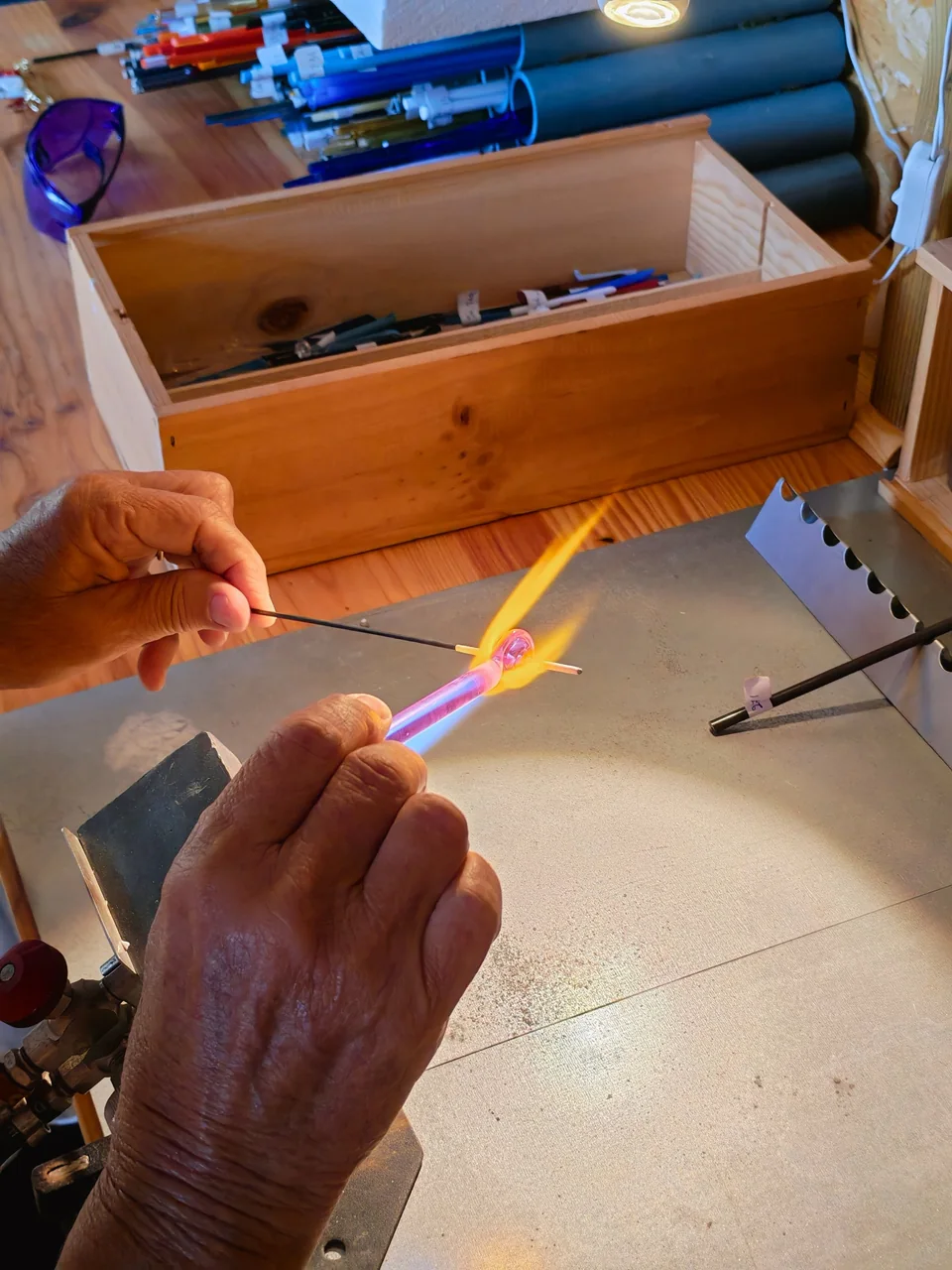 Les mains d'Hélène tiennent une baguette rose dans la flamme du chalumeau.