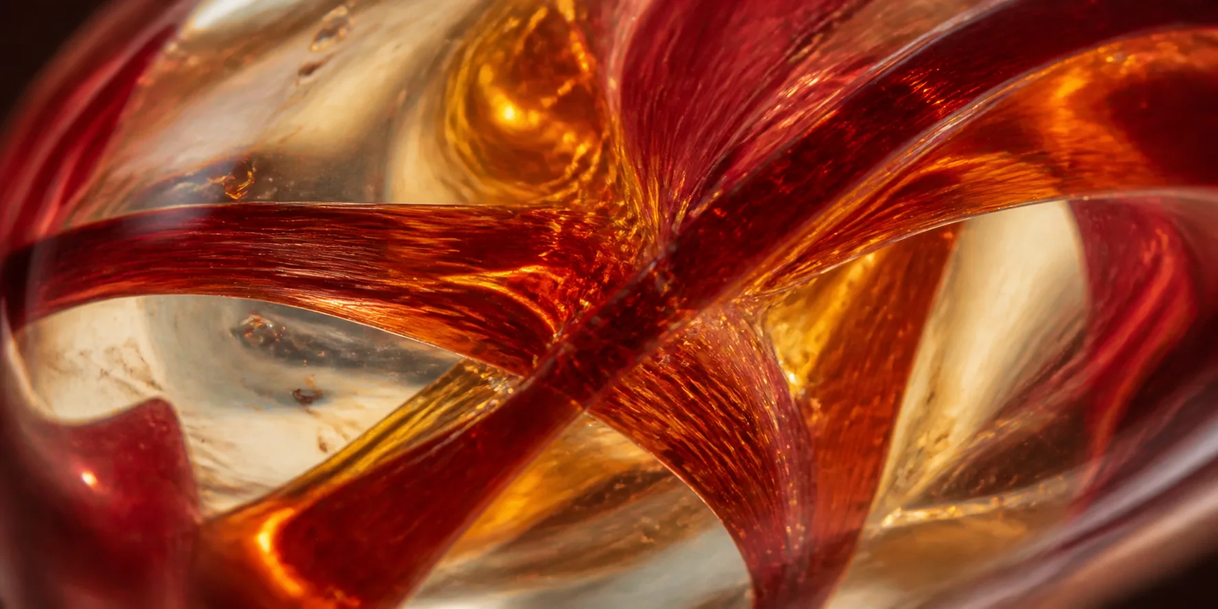 Vu de très près, l'intérieur d'une perle rouge : des rubans de verre rouge et ambre pris dans la masse transparente.